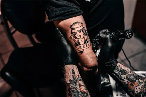 Ein Tätowierer vervollständigt ein "second skin tattoo" einer Frau mit dem Schriftzug "SWEETY" auf einem Arm.