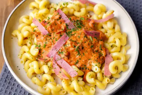 Gedrehte Nudeln mit cremiger Tomatensoße und rosa Wurststreifen, garniert mit Petersilie.