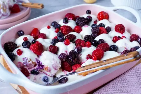 Ein cremiges Windbeutel-Dessert mit frischen Beeren wie Himbeeren, Blaubeeren und Brombeeren in einer rosa Schale.