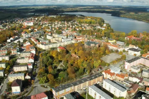 Widok z lotu ptaka na miasto z jeziorem w tle. Widać zabudowania, drzewa w jesiennych barwach i kościół. To największy rynek w Polsce.
