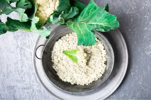 Färdigt blomkålsris i en metallskål, redo för ett hälsosamt blomkålsris recept. En del av ett blomkålshuvud syns ovanför.