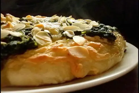 Eine köstliche Spinat Pizza mit knusprigem Teig und gerösteten Mandelblättchen. Dampf steigt auf und verspricht ein warmes, herzhaftes Gericht.