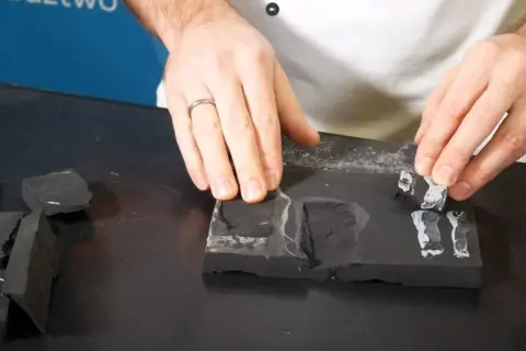 Dłonie układają fragmenty czarnego materiału, przypominającego fartuch EPDM, na ciemnej powierzchni. Montaż wymaga precyzji.