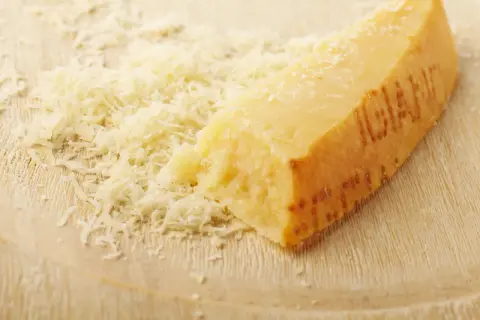 Ein Stück Parmesan mit geriebenem Käse auf einem Holzbrett.