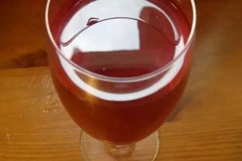 Czerwone wino z róży w kieliszku, na drewnianym stole. Delikatny, rubinowy kolor napoju.