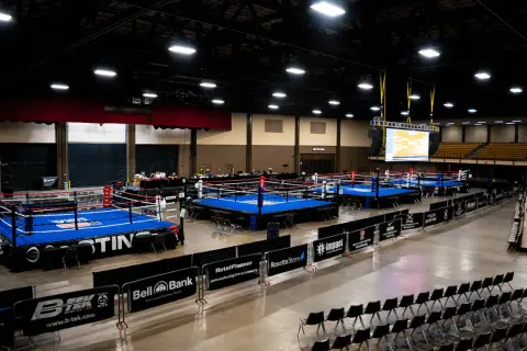 Multiple boxing rings are set up in an arena, ready for competition. A large screen displays a bracket, hinting at the usa boxing weight classes.