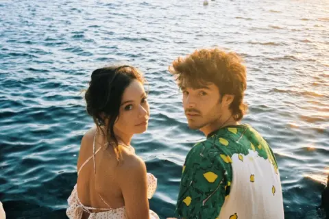 Anna Castillo y Álvaro Mel disfrutan de un atardecer junto al mar, con barcos al fondo.