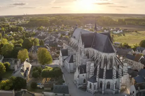 Vue aérienne de la basilique de Cléry-Saint-André au coucher du soleil, baignant le village et ses toits dans une lumière dorée.