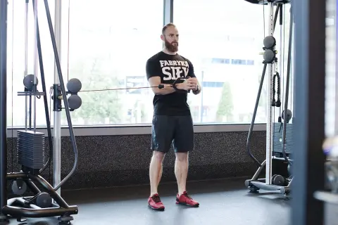 Mężczyzna z brodą wykonuje ćwiczenie pallof press przy użyciu wyciągu.