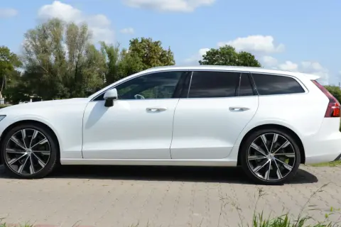 Białe Volvo T6 kombi stoi na tle zieleni i błękitnego nieba.