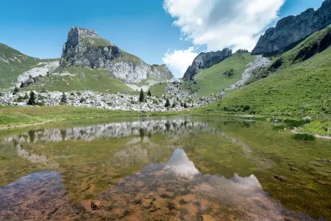 Le lac de Darbon, paisible, reflète les montagnes verdoyantes et rocheuses sous un ciel bleu et nuageux.