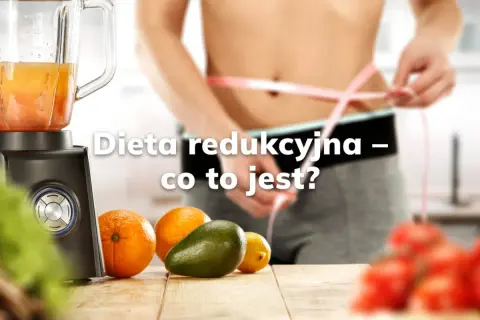 Osoba mierzy talię taśmą. Obok blender, owoce i warzywa. Dowiadujemy się, czym jest redukcja w diecie.