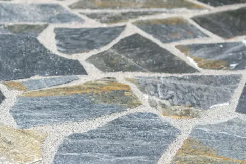 Nahaufnahme von polygonalplatten verlegen. Die unregelmäßigen Steine sind grau und gelblich, mit hellem Sand dazwischen.