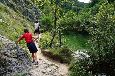 Niños exploran la senda de la hoya de san vicente, junto a un río de aguas cristalinas y vegetación exuberante.