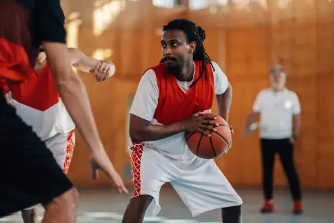 Un joueur de basket concentré, ballon en main, en plein match. Le basket fait-il grandir ? Peut-être pas en taille, mais en esprit d'équipe !
