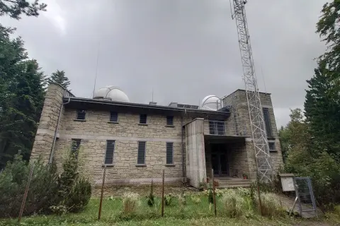 Obserwatorium na Lubomirze, kamienny budynek z kopułami i wieżą telekomunikacyjną, otoczony zielenią.
