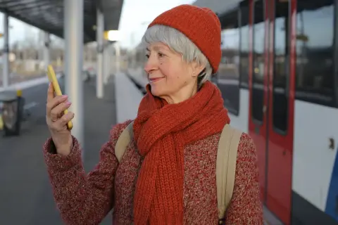 Starsza pani na dworcu sprawdza w telefonie, jak wyrobić kartę seniora PKP.