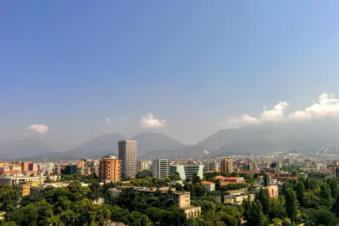 Widok na miasto z górami w tle. Widać nowoczesne budynki i zieleń. To ekuz Albania.