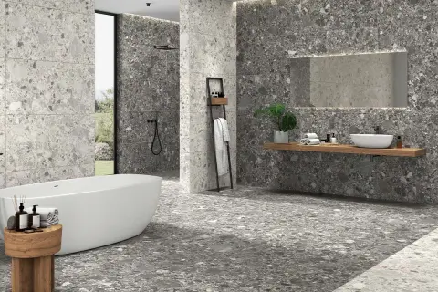 Baño moderno con bañera exenta y lavabo sobre encimera. Las paredes y el suelo muestran diferentes tipos de azulejos con efecto terrazo en tonos grises.