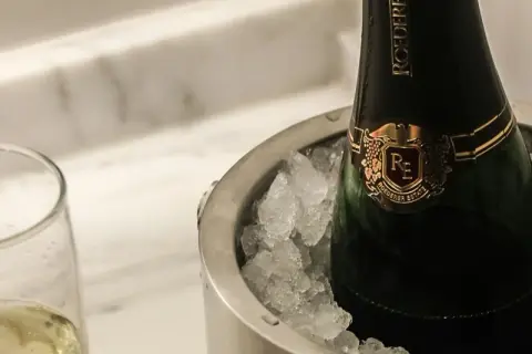 Eine Flasche Champagner in einem Eisbehälter, daneben ein Glas mit prickelndem Wein. Perfekt gekühlt, wann gefriert wein?