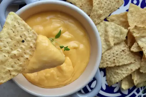 Chrupiące nachos zanurzane w kremowym sosie serowym z serka topionego. Idealna przekąska na imprezę.