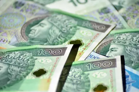 Stos banknotów 100 zł, symbolizujących zasiłek stały. Widać portrety królów i korony.