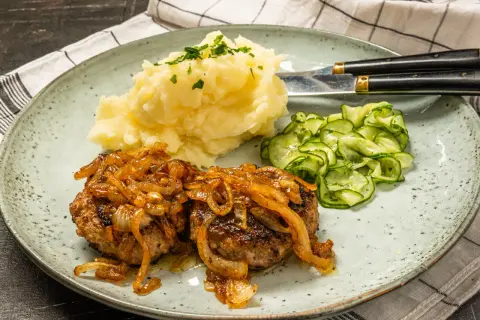 Två saftiga pannbiffar i ugn med karamelliserad lök, serverade med krämigt potatismos och gurksallad. En klassisk svensk rätt.