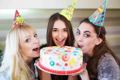 Tre amiche festeggiano con una torta colorata, pronte a soffiare le candeline per un addio al nubilato indimenticabile.