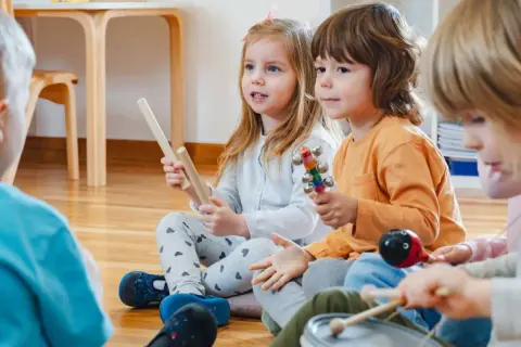 Kinder in der Kita lauschen gespannt einer Klanggeschichte und spielen mit Instrumenten.