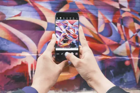 Zdjecie na Instagrama: ręce trzymają telefon, robiąc zdjęcie kolorowego muralu.