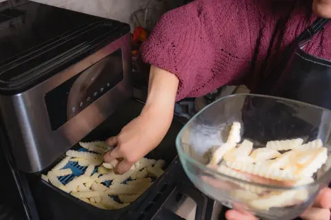 Ręka wkłada frytki do frytkownicy, przygotowując pyszne dania z airfryer przepisy po polsku.