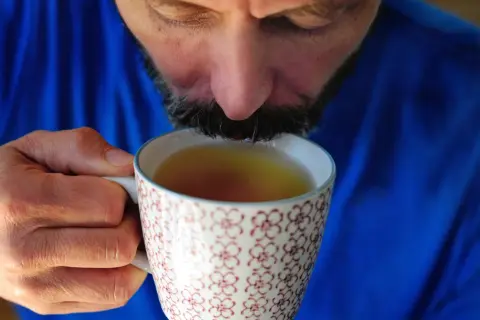 Mężczyzna w niebieskim swetrze pije napar z ziół na refluks z ozdobnego kubka.
