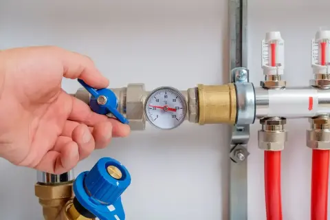 Main d'un homme ajustant la vanne d'un chauffe eau à accumulation. Un thermomètre indique la température.