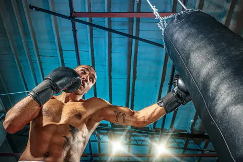 Man i boxningshandskar tränar sparra boxning mot en sandsäck i ett gym.