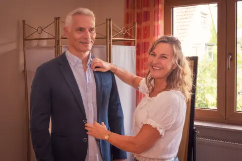Frau hilft Mann beim Anprobieren eines Sakkos. Sie lächelt und richtet den Kragen. Welcher Style passt zu mir?