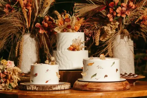 Drei weiße Hochzeitstorten, schlicht elegant dekoriert mit getrockneten Blumen und Blättern, umgeben von herbstlicher Deko.