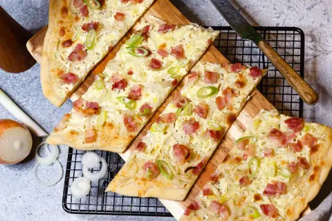 Flammkuchen-Rezept: knuspriger Teig mit Speck, Zwiebeln und Frühlingszwiebeln, bereit zum Genießen.
