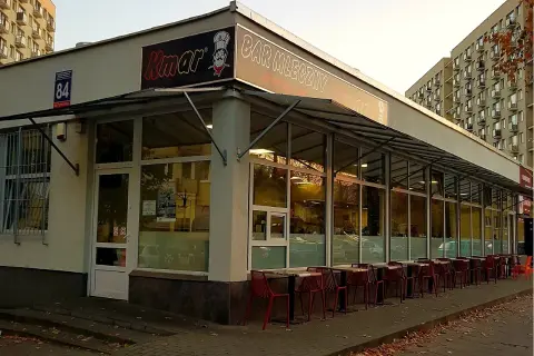 Bar mleczny Kmar z czerwonymi krzesłami przed wejściem.