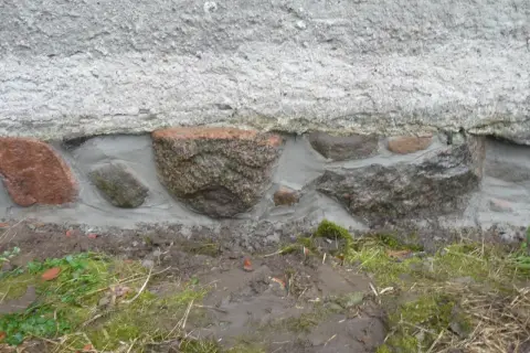 Das Feldsteinfundament wird mit Mörtel abgedichtet. Große Steine sind sichtbar, umgeben von frischem Mörtel, der die Lücken füllt.