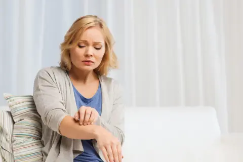 Donna si gratta il braccio, sofferente per l'aria secca che le irrita la pelle.