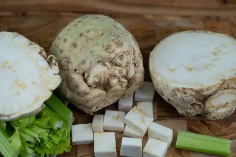Knollensellerie-Rezepte für eine herzhafte Hauptspeise: Ein ganzer Knollensellerie, halbiert und gewürfelt, mit Staudensellerie auf Holzuntergrund.