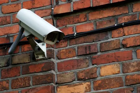Caméra de surveillance blanche fixée sur un mur de briques. Comment reconnaître une caméra factice ? Cherchez l'absence de câbles ou de voyants lumineux.