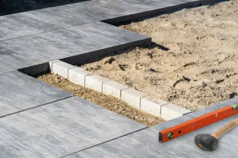 Układanie płyt tarasowych na suchym betonie. Widać poziomicę i gumowy młotek, narzędzia do precyzyjnego montażu.