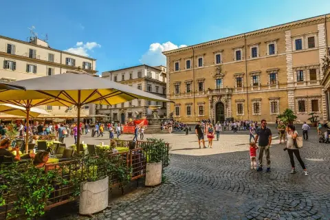 Piazza animata con persone che passeggiano e si godono un caffè all'aperto, un assaggio delle serate Erasmus a Roma.