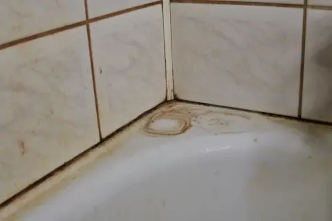 Coins de baignoire sales, avec des traces de javel sur le carrelage et des auréoles sur le blanc.