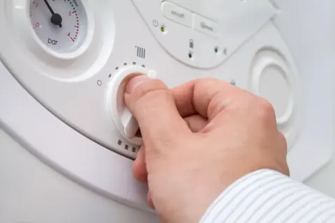 Mano che regola la temperatura caldaia termosifoni. Quadrante bianco con simboli di riscaldamento e manopola.