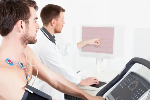 Un homme subit un test d'effort dangereux sur un tapis roulant, des électrodes sur la poitrine, tandis qu'un médecin surveille son rythme cardiaque sur un écran.