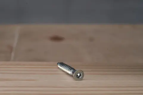 Metalowy konfirmat leży na drewnianym blacie.