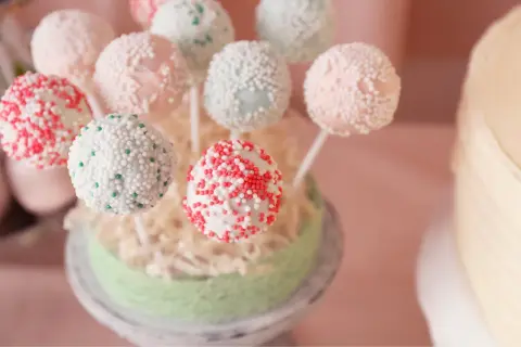 Bunte Kuchen am Stiel, verziert mit Perlen und Streuseln, auf einem grünen Podest arrangiert.