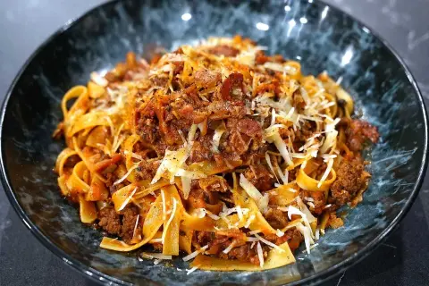 En skål med breda bandnudlar täckta av en mustig köttfärssås, toppad med riven ost och peppar. En härlig pasta ragu!